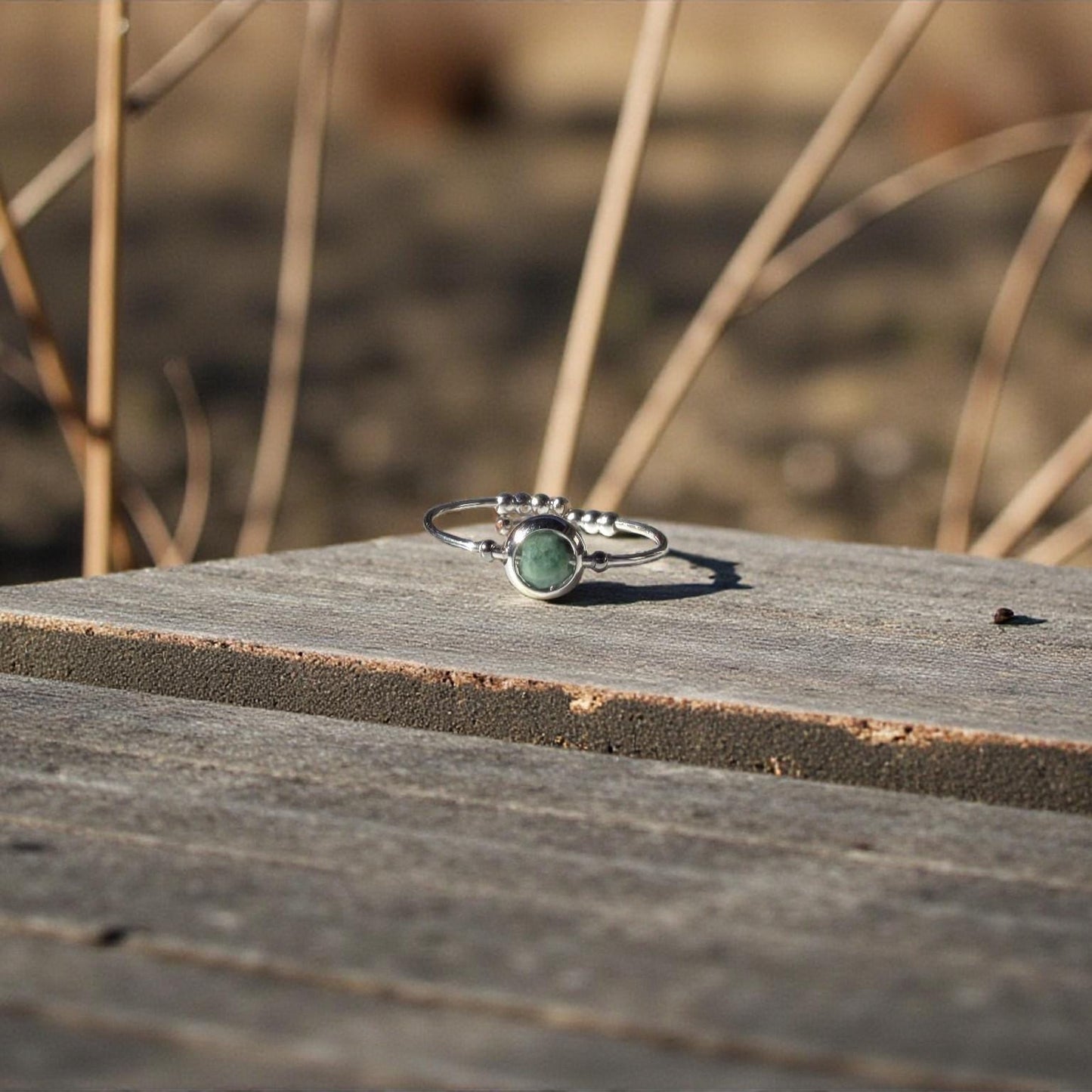 Silver ring with a green emerald gemstone on a wooden surface with blurred natural background