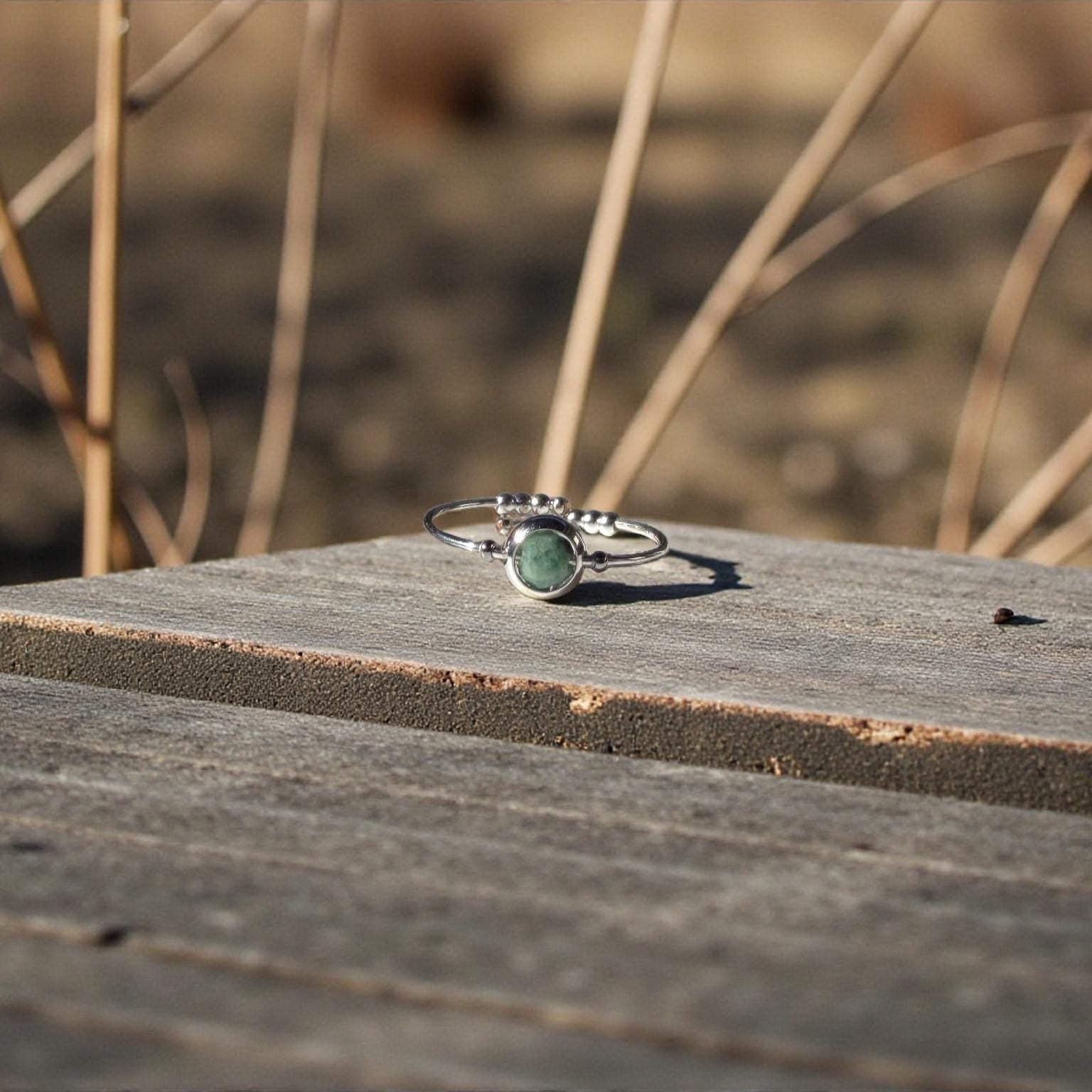 Silver ring with a green emerald gemstone on a wooden surface with blurred natural background