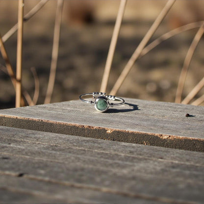 Silver ring with a green emerald gemstone on a wooden surface with blurred natural background
