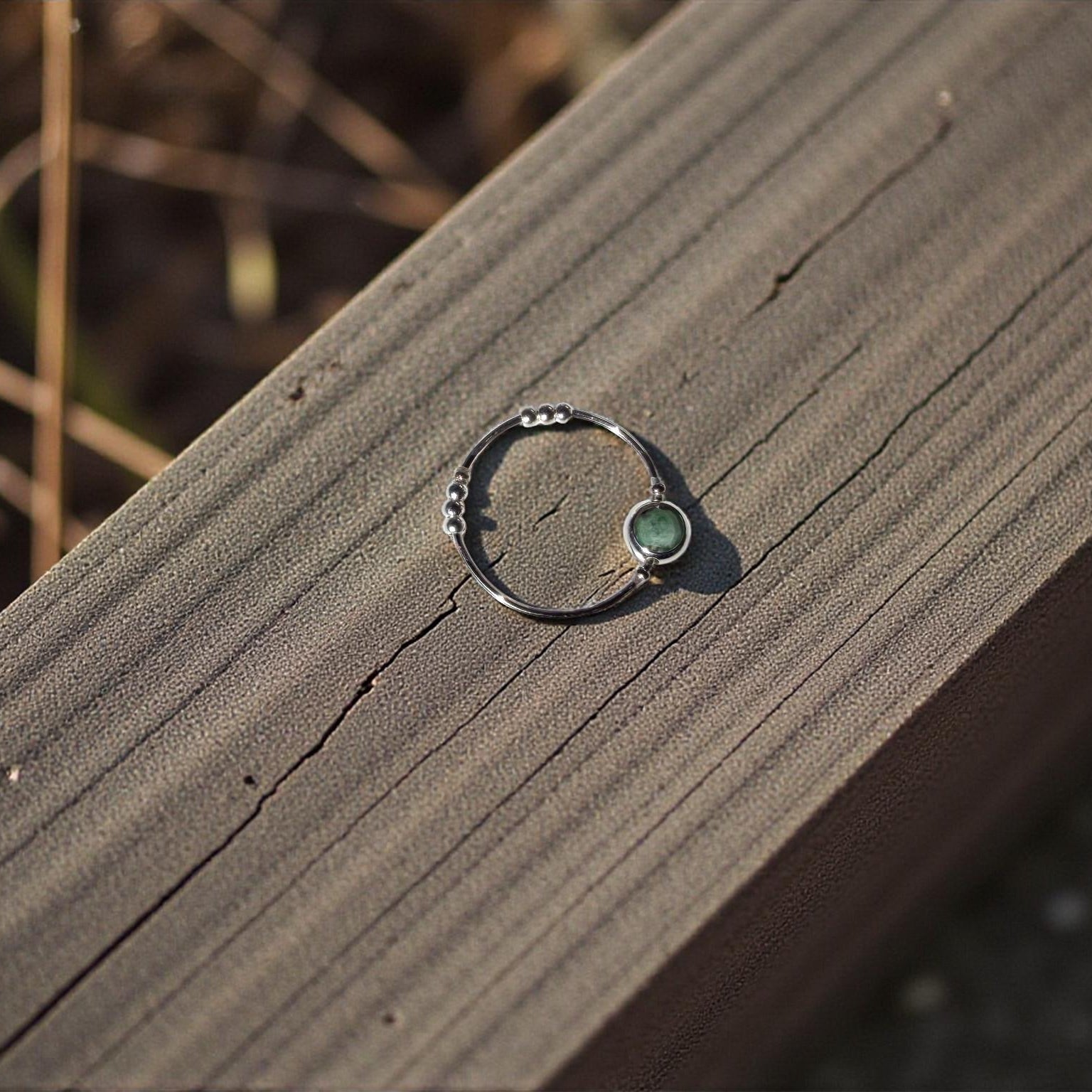 Silver ring with a green emerald stone on a wooden surface