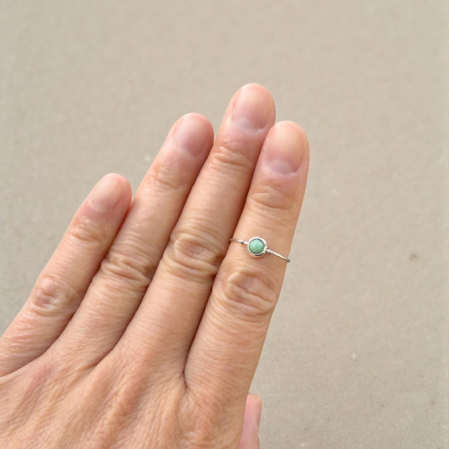 Hand wearing a natural emerald ring with a green gemstone on a beige background