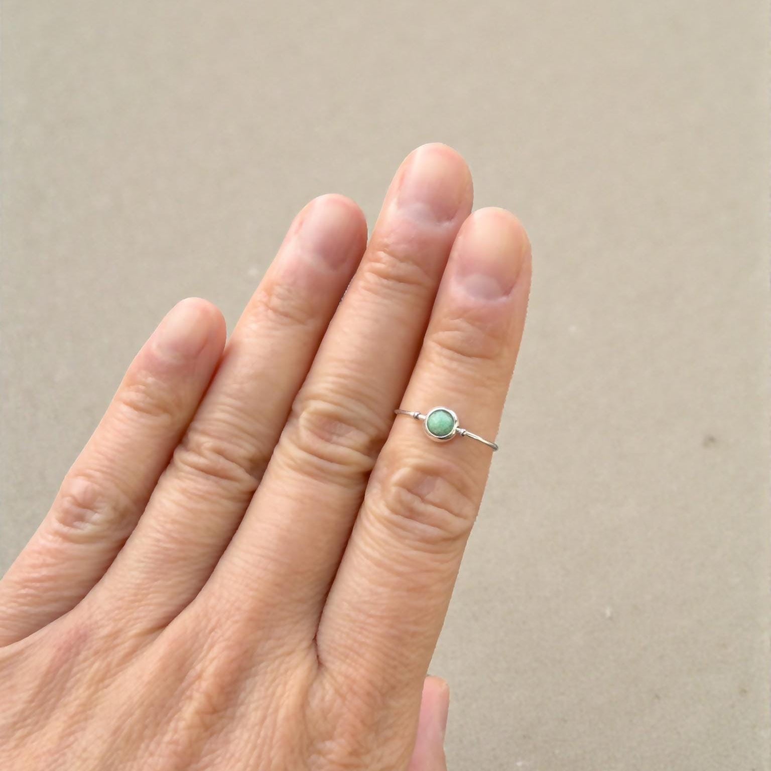 Hand wearing a natural emerald ring with a green gemstone on a beige background