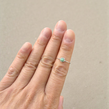 Hand wearing a natural emerald ring with a green gemstone on a beige background