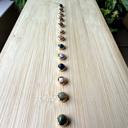 Row of gold-framed jewelry on a light wooden surface